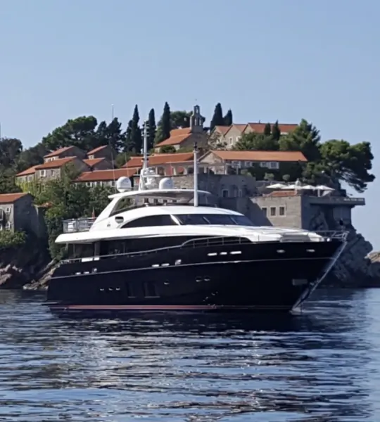 Luxury black and white yacht on calm blue water with coastal town and red-roofed buildings in the background