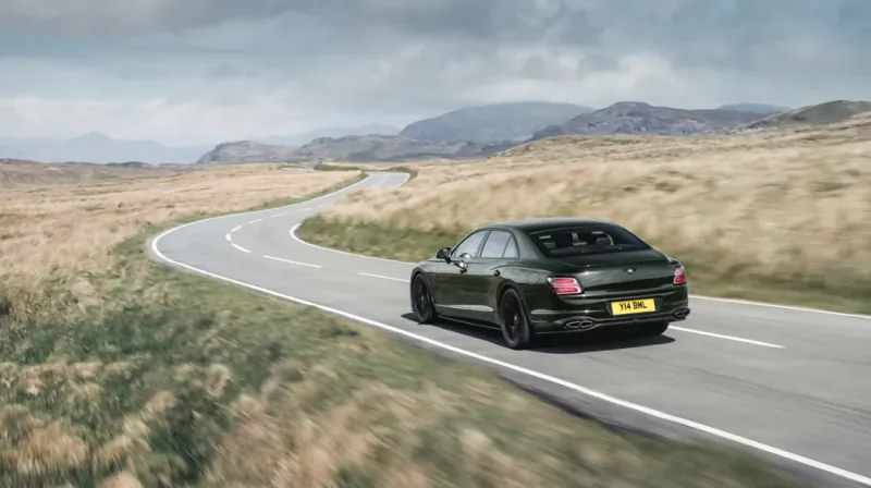 Dark green Bentley Flying Spur sedan driving on a winding mountain road