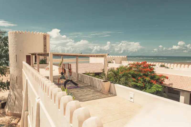 People practicing yoga on a rooftop terrace overlooking the ocean at The Fort Shela Kenya villa