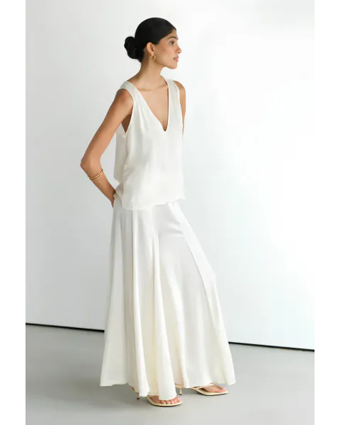 Woman in white satin V-neck top and flowing wide-leg pants posing in studio