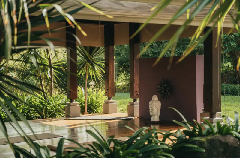 Covered patio with Buddha statue, sunburst wall art, and lush tropical garden view