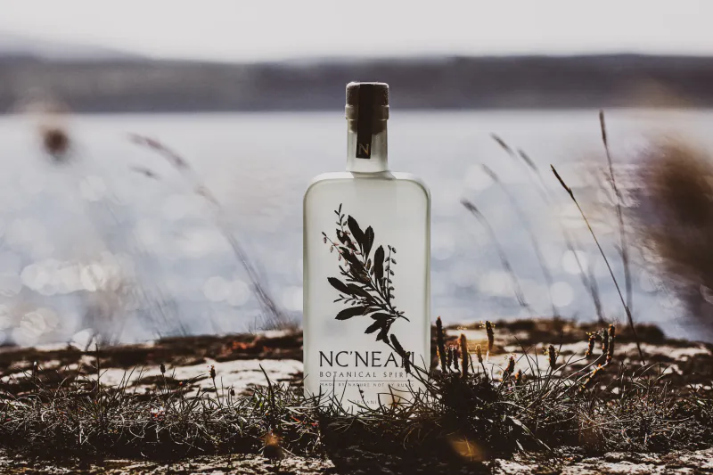 NC'NEAN Botanical Spirit bottle standing on grass by a lake