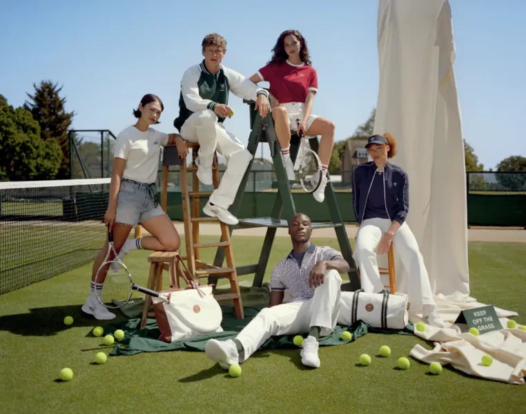Group of diverse models posing with tennis gear on a sunny Wimbledon court, surrounded by balls, bags, and a 'Keep Off The Grass' sign