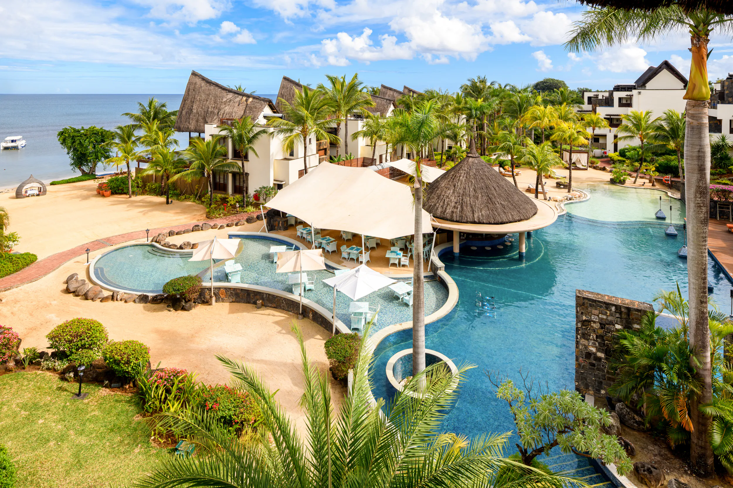 Aerial view of Le Jadis Beach Resort & Wellness Mauritius with thatched-roof villas, multiple pools, palm trees, and oceanfront beach