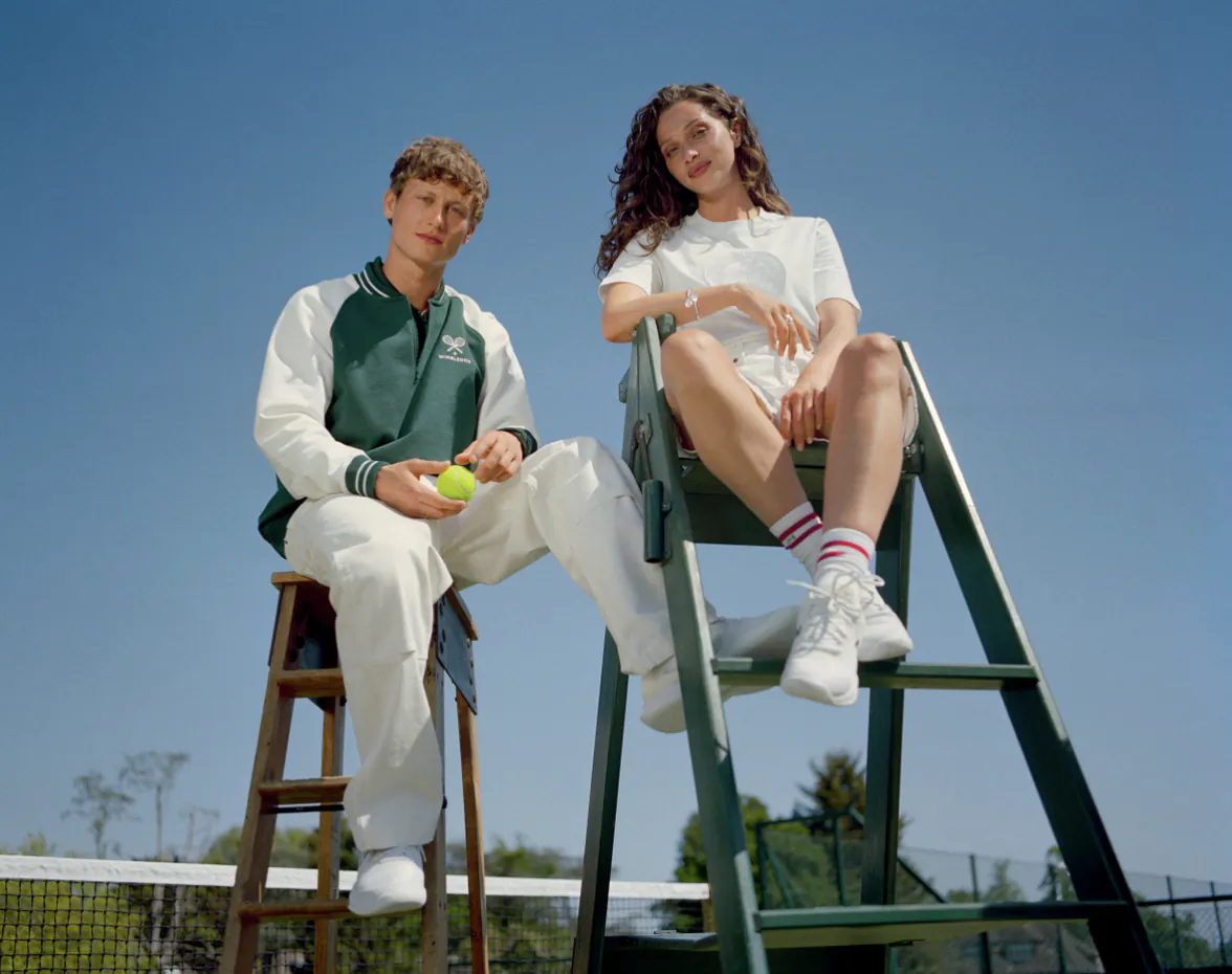 Young man and woman posing on tennis court with umpire chair, man holding tennis ball