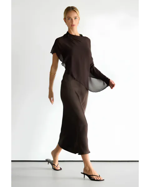 Woman in brown satin top and midi skirt posing against white studio backdrop