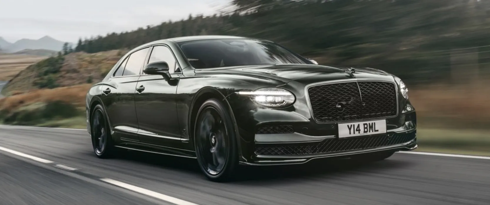 Dark green Bentley Flying Spur sedan driving fast on a scenic road with motion blur