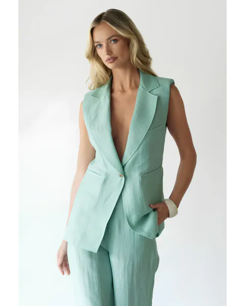Blonde woman in a sleeveless mint green linen blazer and matching trousers, posing with one hand in her pocket