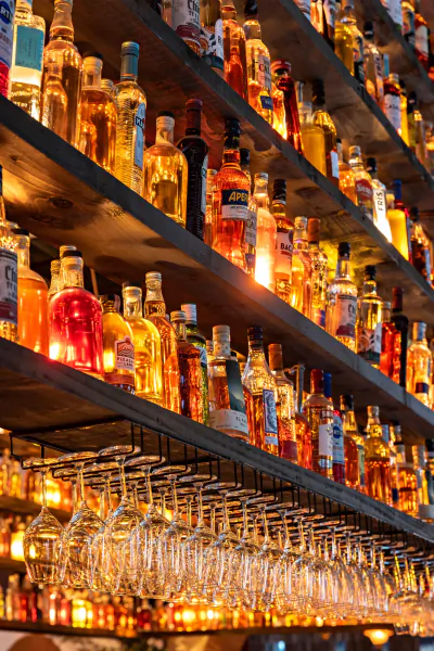Wooden shelves lined with colorful liquor bottles and rows of hanging wine glasses in a bar