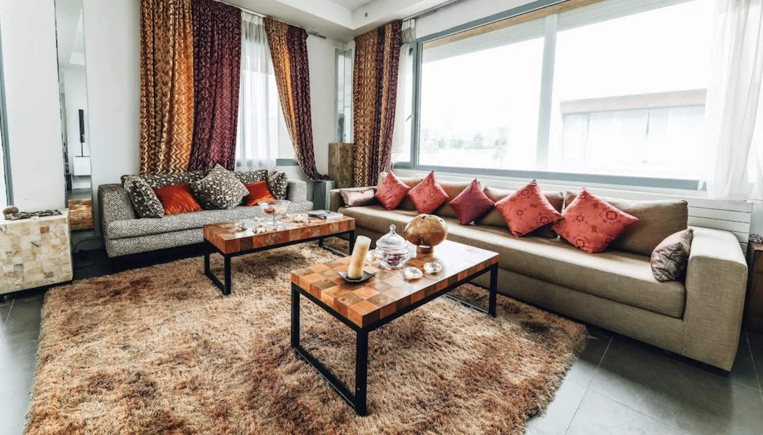 Modern living room with two sofas, wooden coffee tables, and a large shaggy brown rug on a tiled floor