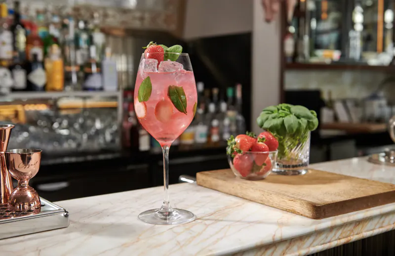Strawberry basil cocktail in a wine glass on a marble bar with fresh berries and basil