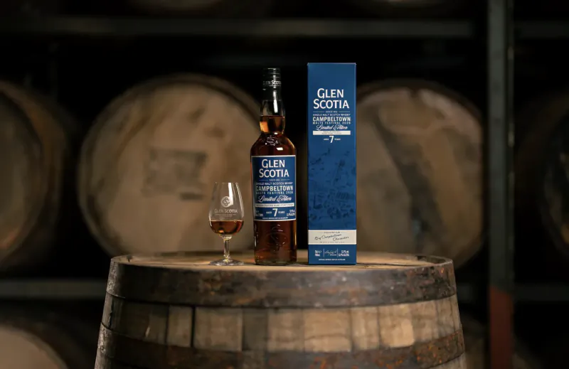 Glen Scotia Campbeltown 7 Year Old whisky bottle, box, and glass on a wooden barrel in a distillery warehouse