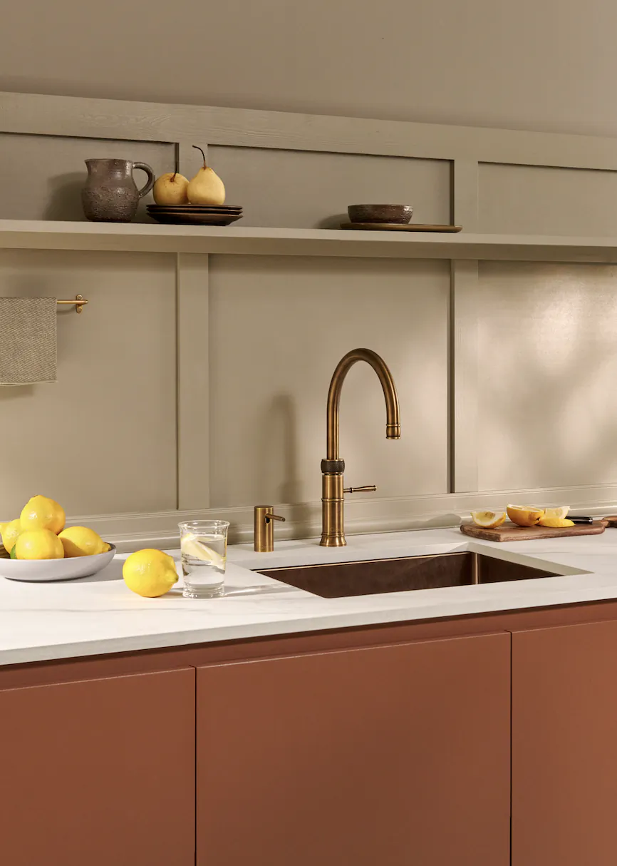 Modern kitchen with brushed gold Quooker faucet, white countertop, terracotta cabinets, bowl of lemons and glass of water