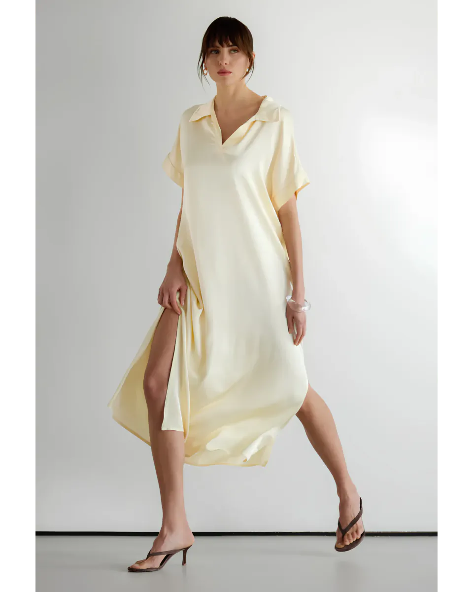 Woman in pale yellow satin midi dress with side slit and short sleeves, posing against white studio backdrop