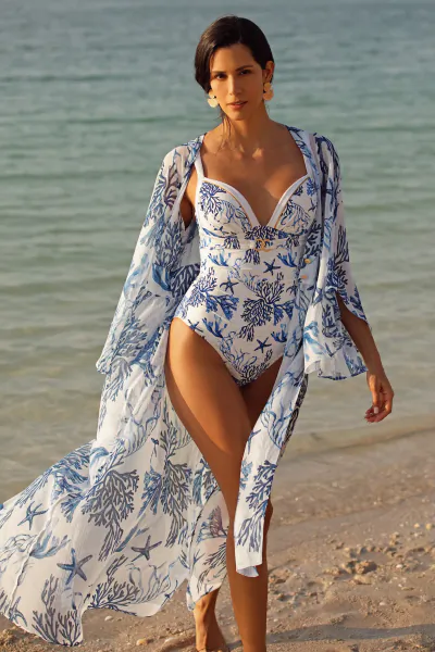Woman in blue and white patterned swimsuit and flowing cover-up walking on a sunny beach at golden hour