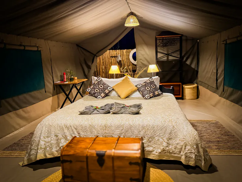 Cozy luxury tent interior with large bed, patterned pillows, lamps, wooden trunk, and canvas walls