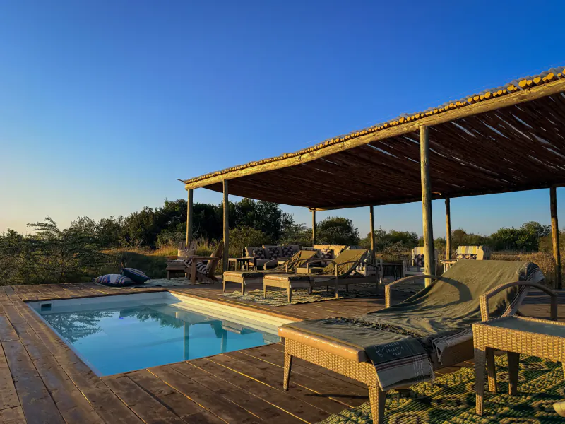 Luxury outdoor pool deck with lounge chairs under a thatched wooden pergola at sunset