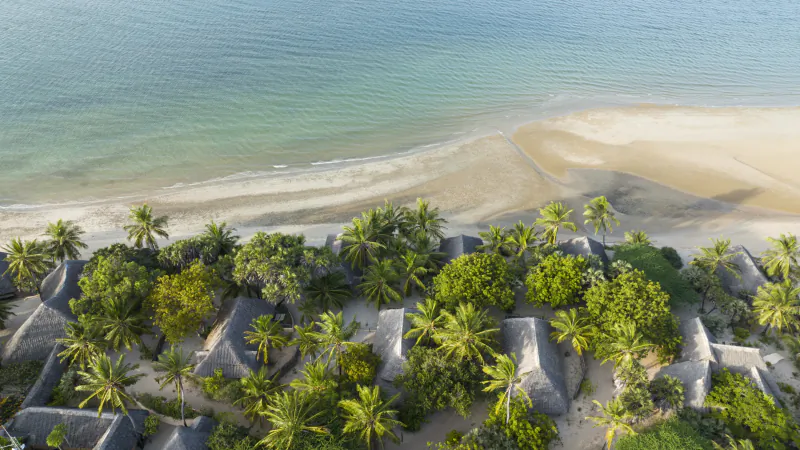 Aerial view of Manda Bay Lodge on Manda Island, Kenya, showing thatched-roof bungalows nestled among palm trees along a sandy beach and turquoise ocean