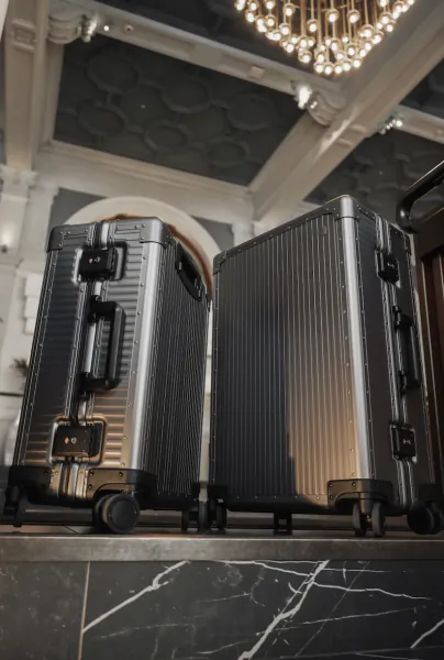 Two sleek black hard-shell suitcases standing side by side on a marble surface in an elegant lobby with a crystal chandelier overhead