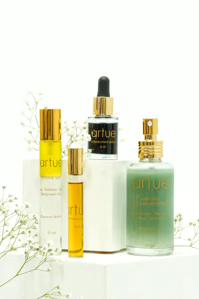 Artue skincare bottles with gold caps and dropper on white blocks with baby's breath flowers