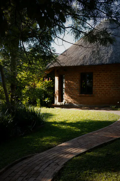 Brick lodge with thatched roof and winding path through lush garden at Lilayi Lodge, Zambia