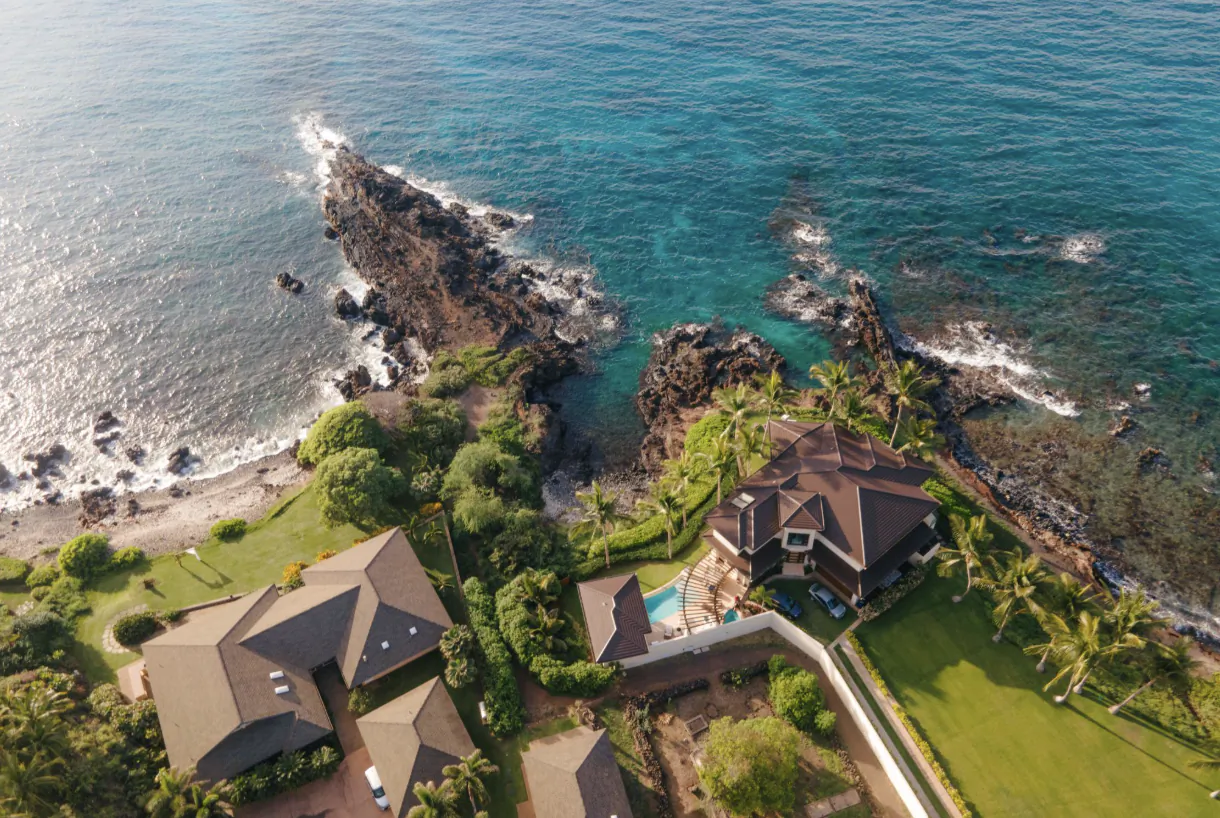 Aerial view of luxury oceanfront homes with pools on a rocky Hawaiian coastline
