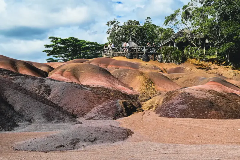 Colorful striped sand dunes at Mauritius viewpoint with tourists on wooden deck overlooking the landscape