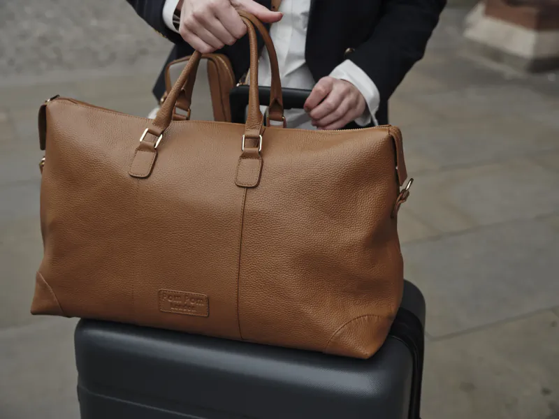 Person in a suit holding a brown leather duffel bag on a black suitcase