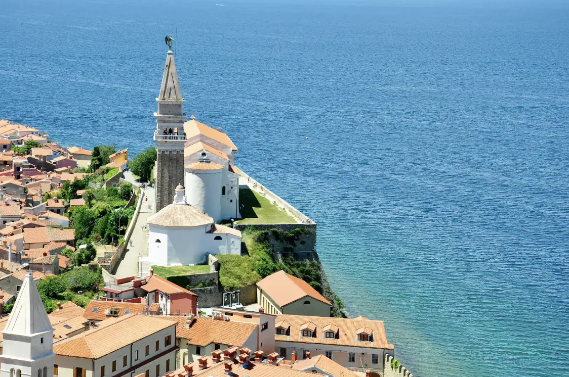 Aerial view of a historic coastal town with a tall stone bell tower overlooking the blue sea