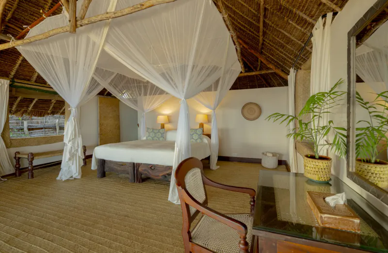Luxury bedroom at Manda Bay Lodge with four-poster bed draped in white mosquito netting, thatched roof, and wooden furniture