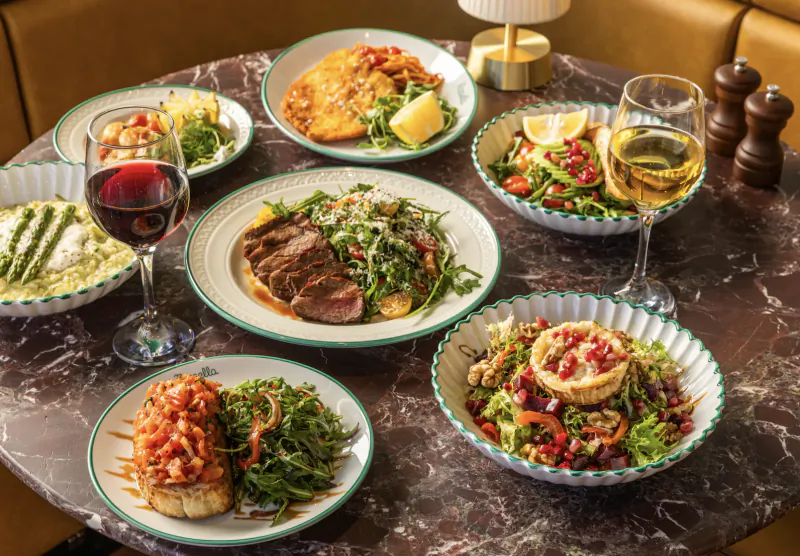 Table of Italian dishes including steak salad, bruschetta, tart, pasta, wine glasses on marble table