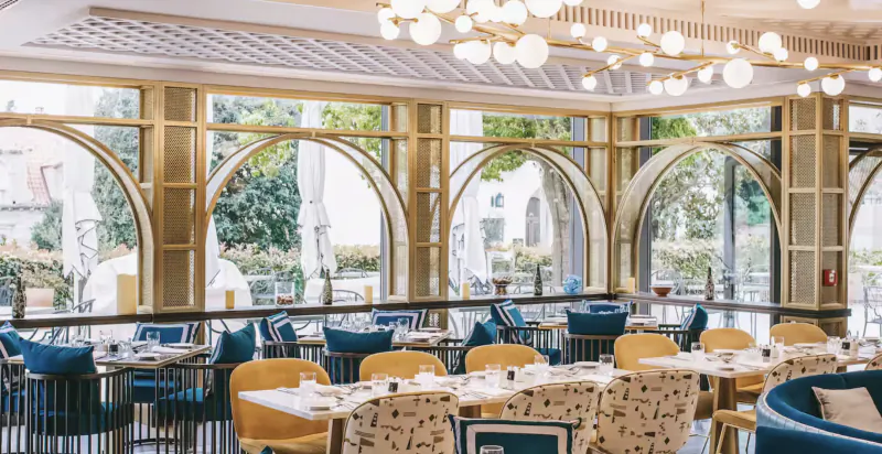 Elegant hotel restaurant interior with arched windows, colorful chairs, and city view