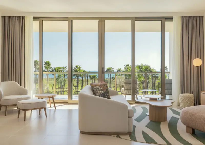Bright modern living room with white sofa, armchairs, and large windows overlooking ocean and palm trees at The Westin Salgados Beach Resort