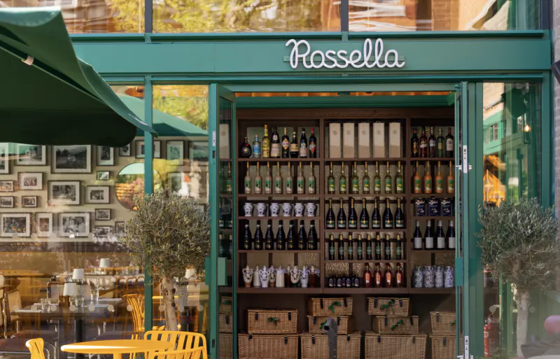 Rossella storefront with open green doors displaying rows of wine bottles and wicker baskets