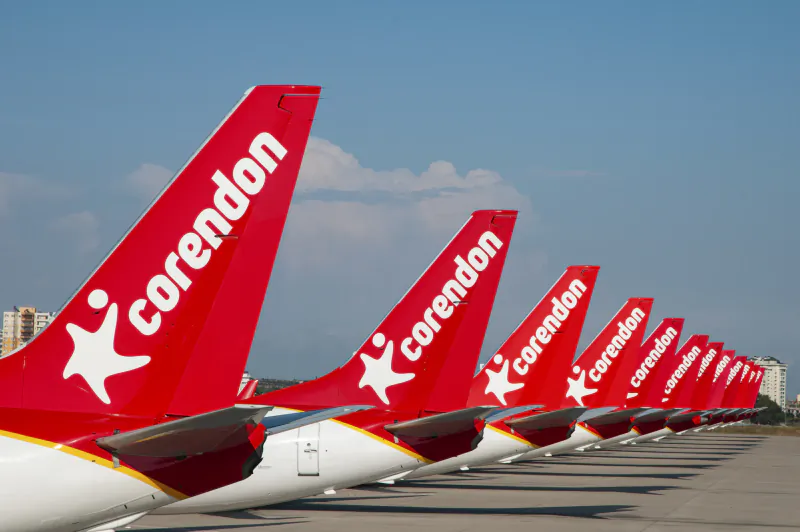 Row of Corendon Airlines red airplane tails lined up on the tarmac, each showing the white logo and text