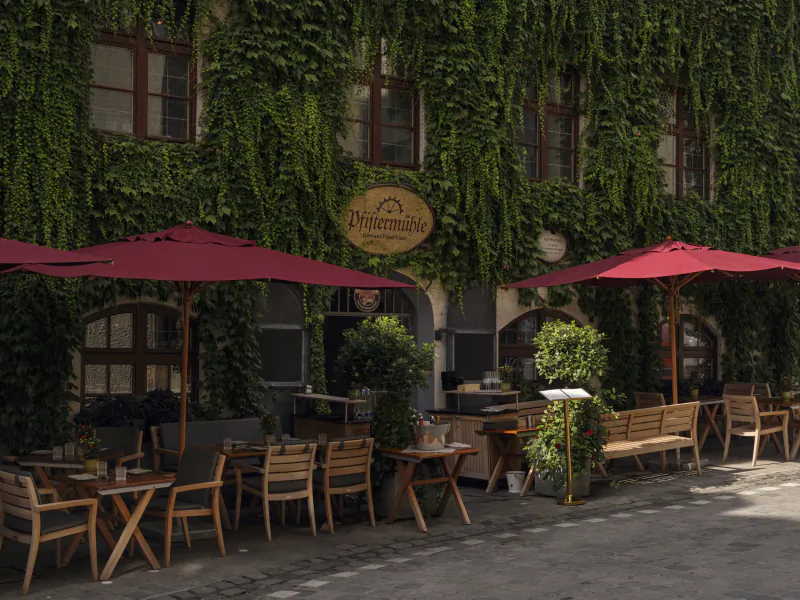 Outdoor patio of Platzl Hotel Munich with red umbrellas, wooden tables, and ivy-covered building facade