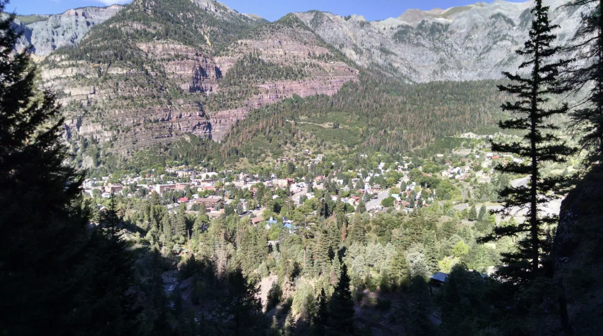 Aerial view of a mountain town nestled in a forested valley with rocky peaks rising behind