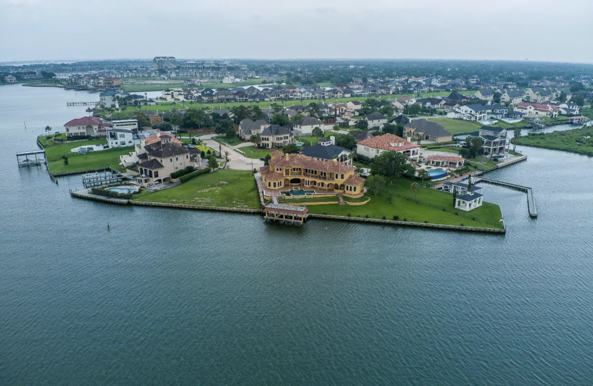 Aerial view of luxury waterfront homes on a small island surrounded by water, with docks and green lawns