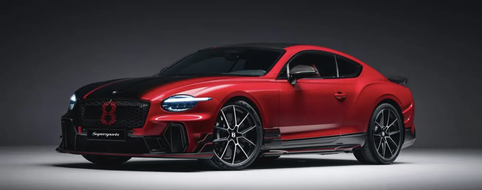 Red and black two-door sports coupe with glowing headlights and black alloy wheels on a studio background