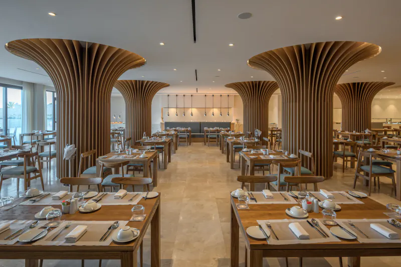 Modern restaurant interior with large wooden sculptural columns, set dining tables, and pendant lights