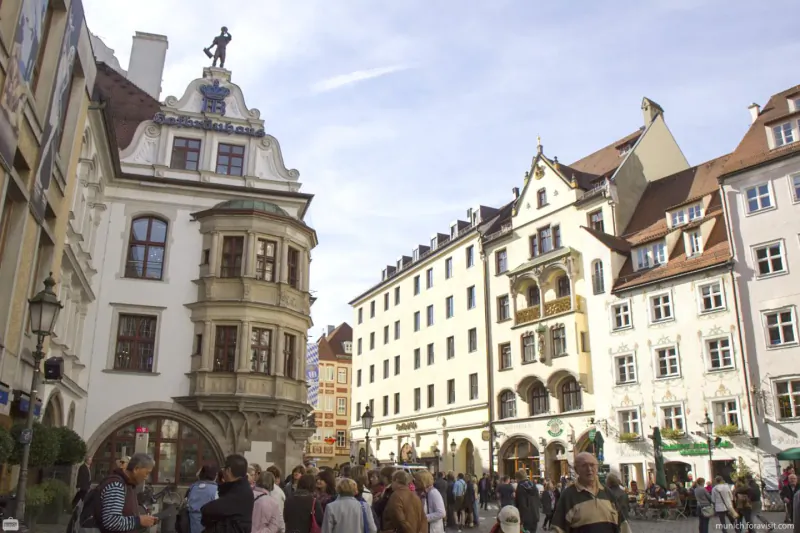 Historic buildings and crowd in Munich's Platzl square with ornate facades and a rooftop statue