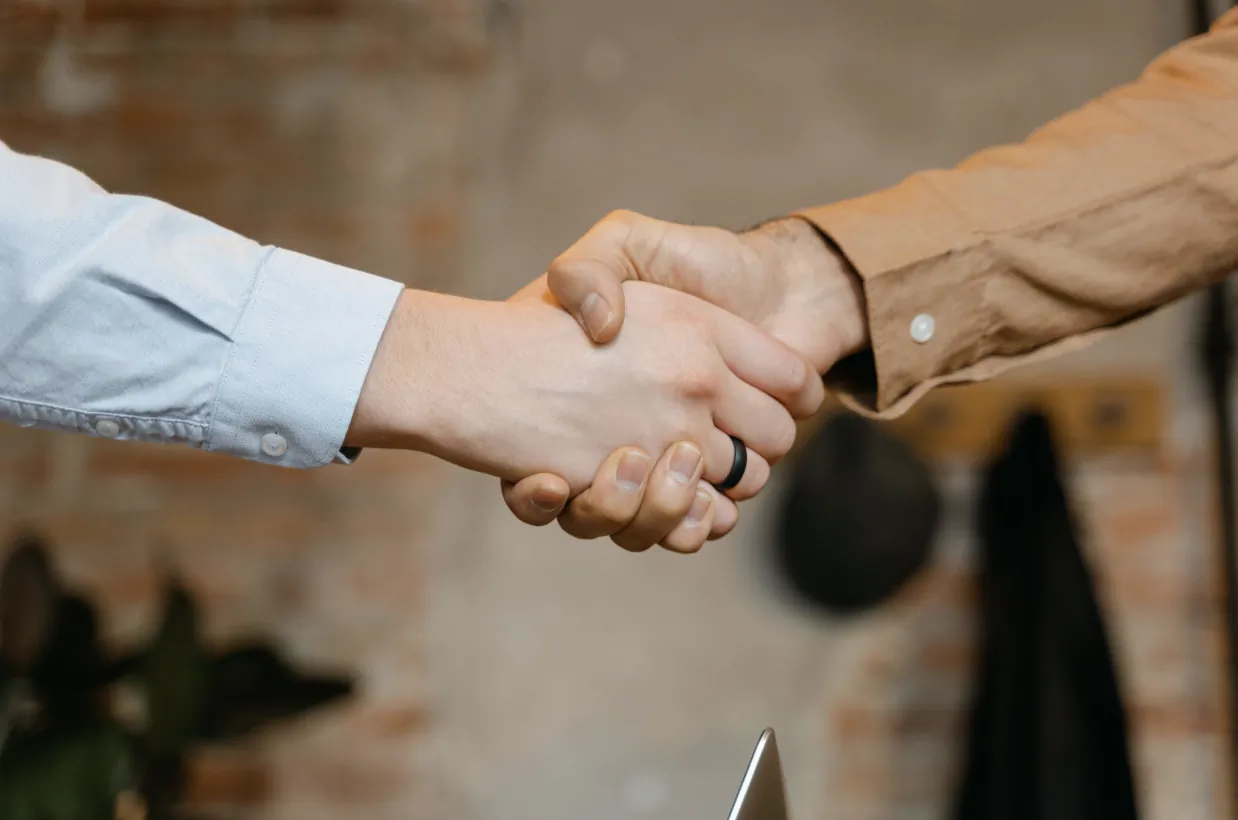 Two people shaking hands in a professional setting, one wearing a black ring