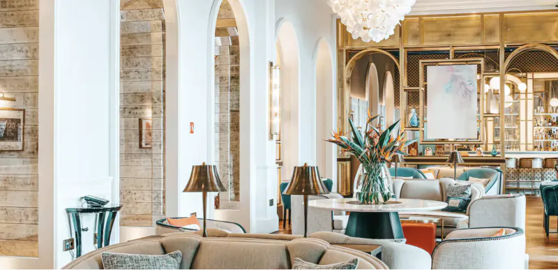 Elegant hotel lobby with arched doorways, modern seating, floral centerpiece, and gold bar area