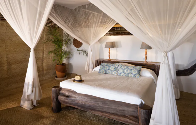 Four-poster wooden bed with white canopy and blue pillows in a rustic Kenyan lodge bedroom
