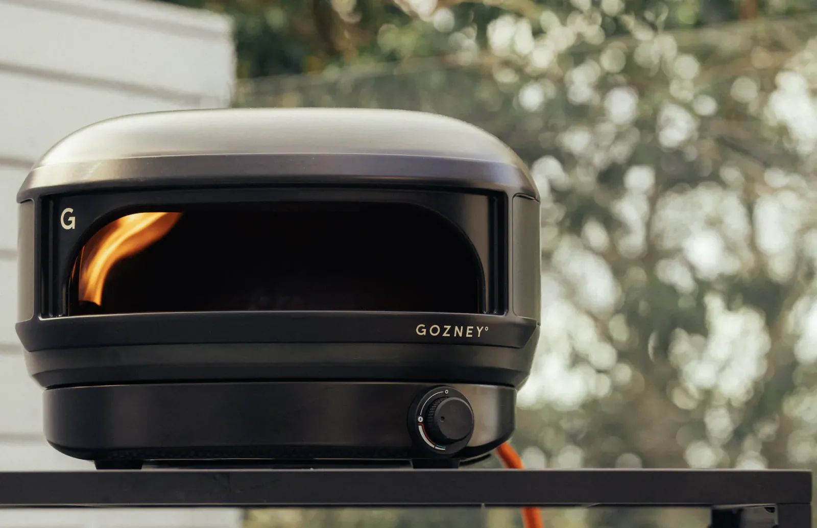 Gozney Arc Lite pizza oven with visible flame inside, black compact design on outdoor table