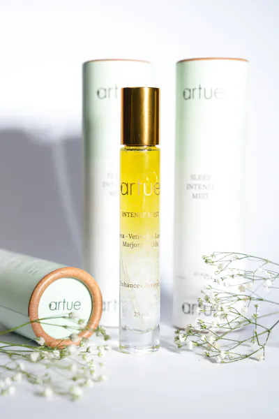 Artue Intense Pulse perfume bottle with gold cap, surrounded by product boxes and white flowers