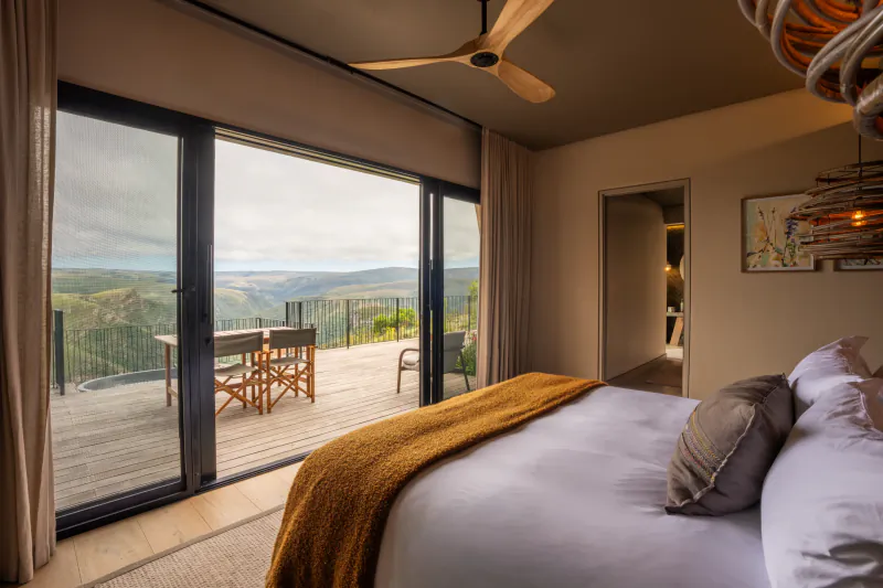 Modern bedroom with large sliding glass doors opening to a wooden deck and scenic mountain valley view