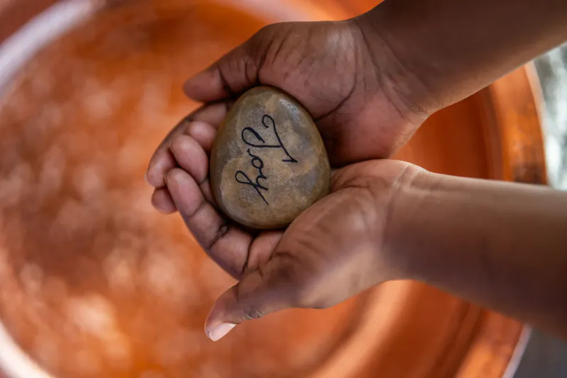 Two hands gently holding a smooth stone with the word 'Joy' written on it