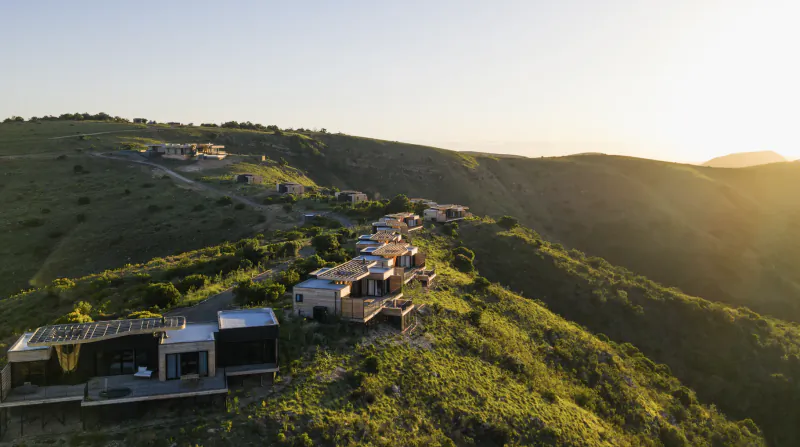 Aerial view of modern hillside villas with solar panels on a green slope at sunset