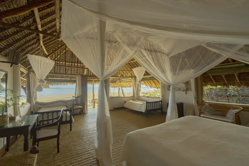 Luxury beachfront bedroom at Manda Bay Lodge with four-poster bed draped in white mosquito netting, thatched roof, and ocean view